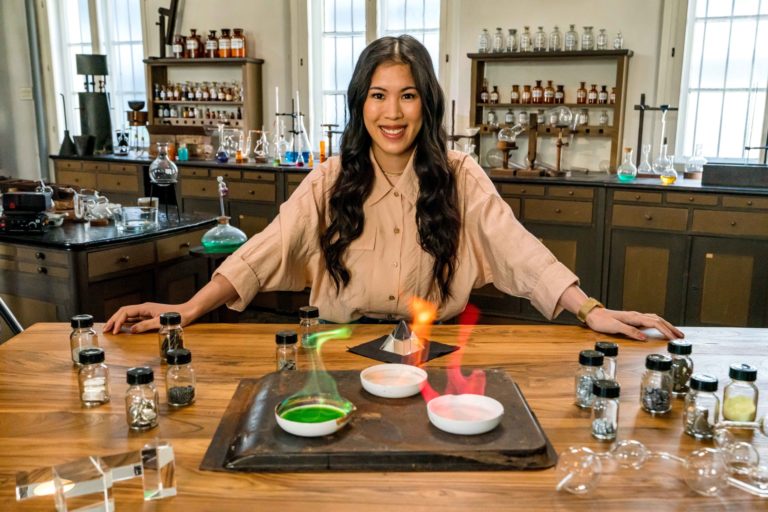 "Terra X: - Wunderwelt Chemie - Die Bausteine der Natur": Mai Thi Nguyen-Kim lehnt in einem alten Labor an einem Tisch. Vor ihr verschiedene Schalen mit chemischen Stoffen, die in grün, rot und gelb leuchten.